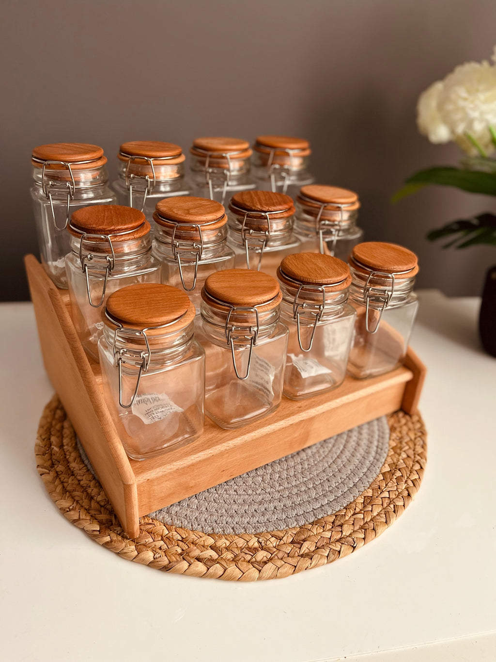 Wooden stairs-style tiered spice rack holding 12 clear 300ml airtight glass jars with stainless steel clip-top lids and rubber seals