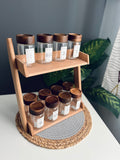 Wooden tiered kitchen counter shelf organizer displaying 12 large clear 300ml glass spice jars with custom labeling stickers