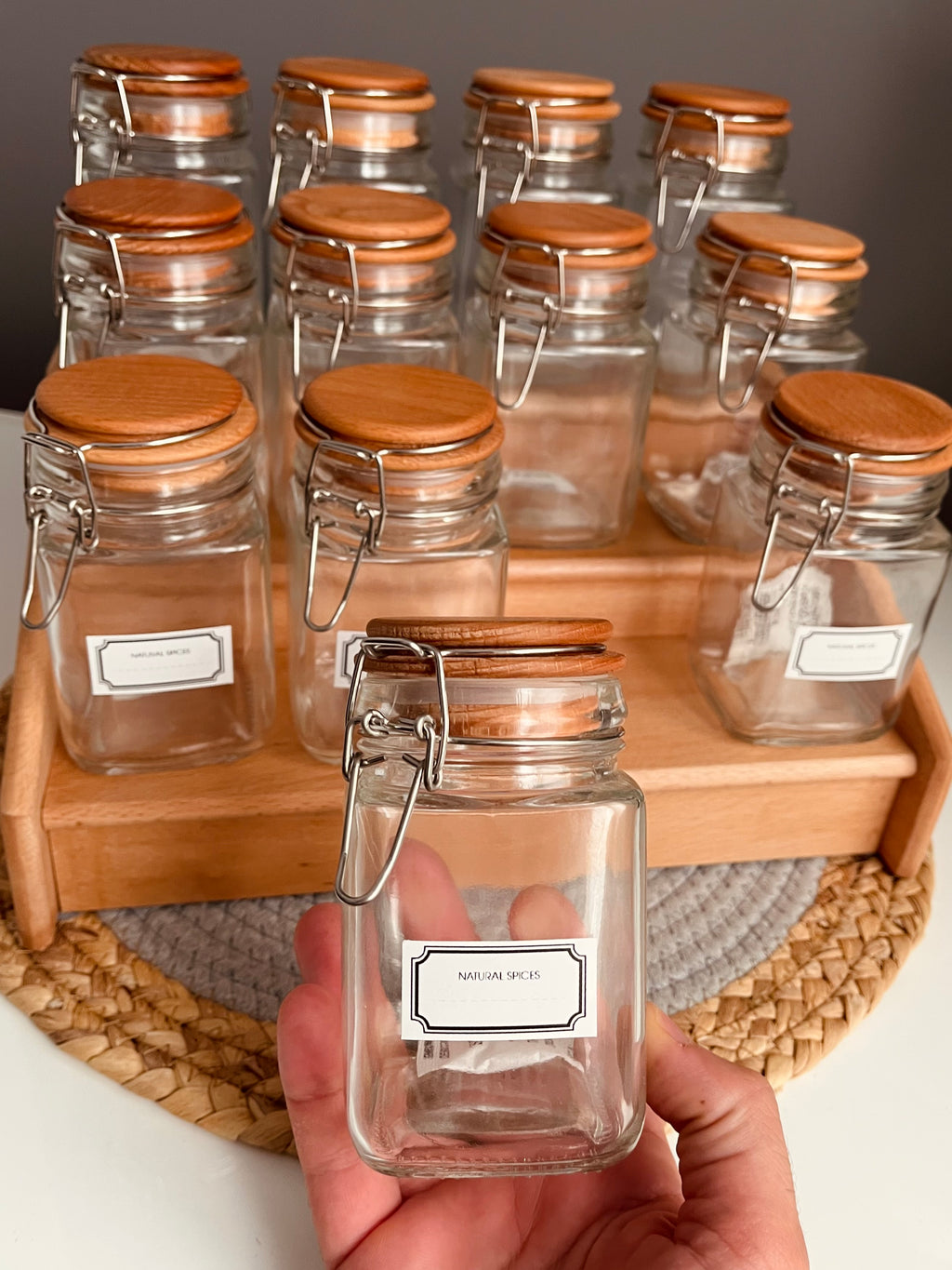 Wooden stairs-style tiered spice rack holding 12 clear 300ml airtight glass jars with stainless steel clip-top lids and rubber seals