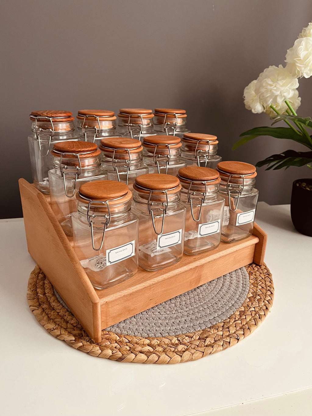 Wooden stairs-style tiered spice rack holding 12 clear 300ml airtight glass jars with stainless steel clip-top lids and rubber seals